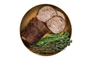 Slices of roasted stuffed pork meat roulade on a plate with rosemary and thyme. Isolated on white background. photo
