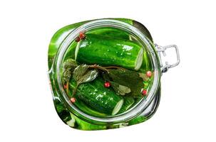 Green salted cucumbers in a glass jar. Canned vegetables. Isolated on white background. Top view. photo