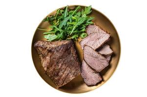 Roast Tri Tip or sirloin bottom beef steak on a plate with arugula. Isolated on white background. photo