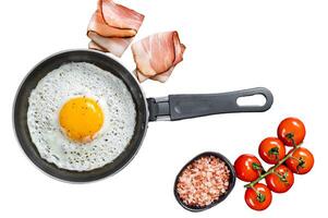 Fried egg in a frying pan with tomatoes and bacon. Isolated, white background. photo