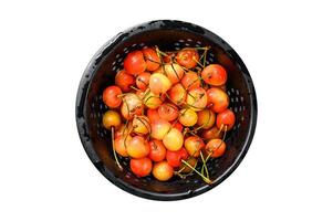 Mix of yellow and red ripe cherries in a colander. Isolated, white background. photo