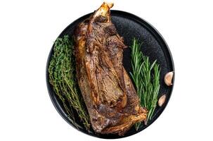 Roasted lamb mutton shoulder meat on a plate with knife and fork. Black background. Top view photo