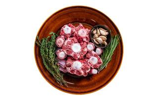 Fresh uncooked beef Oxtail cut Meat on rustic plate with herbs. Isolated on white background. photo