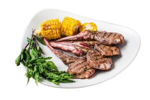 Grilled lamb chops steaks in a plate with corn and tomato. Isolated on white background, top view. photo