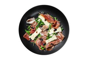 Prosciutto crudo ham salad with brie camembert cheese and arugula on a plate. Isolated on white background. photo