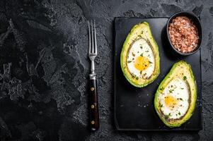 Eggs baked in avocado with herbs and spices. Black background. Top view. Copy space photo