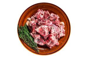 Raw mutton meat diced for goulash or stew with bone on a rustic plate. Isolated on white background. photo