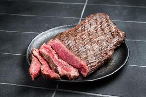 Grilled Flap or Flank Steak, sliced on a plate. Black background. Top view photo