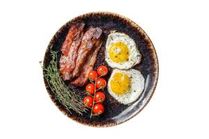 Breakfast with fried eggs and bacon with herbs in plate. Isolated, white background. Top view. photo
