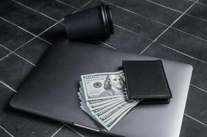 Corporate business desktop with laptop, digital tablet, wallet, money and cup of coffee. Black background. Top view. Copy space photo