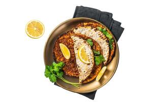 Turkish lahmacun pizza with mince meat and tomatoes on a plate with parsley and lemon. Isolated, white background. photo