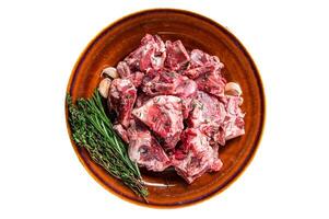 Raw mutton meat diced for goulash or stew with bone on a rustic plate. Isolated on white background photo