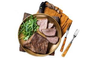 Roast Tri Tip or sirloin bottom beef steak on a plate with arugula. Isolated, white background. photo