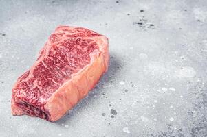 Raw Wagyu striploin or New york steak on a butcher table. Gray background. Top view. Copy space photo