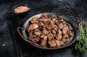 Fried chicken liver with onions and herbs. Black background. Top view photo