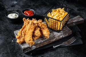 Chicken breast strips with French Fries and Ketchup. Black background. Top view photo