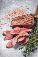 Roast sliced Flank or Flap Steak on a butcher cleaver with thyme and pink salt. Gray background. Top view photo