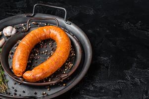 Smoked sausage with thyme and spices in a steel tray. Black background. Top view. COpy space photo
