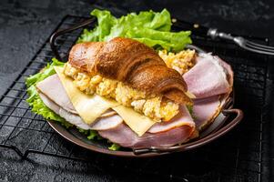 Breakfast croissant sandwich with scrambled eggs, cheese and ham. Black background. Top view photo