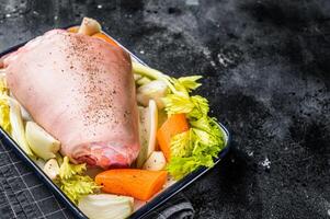 Cooking of Schweinshaxe from Raw pork shank knuckle with vegetables and herbs. Black background. Top view. Copy space photo