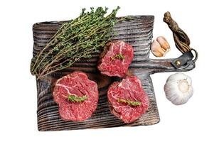 Prime raw Fillet mignon steaks on a wooden board with thyme and garlic Isolated on white background, top view. photo