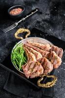 Grilled Lamb mutton Chops steaks in a skillet with green salad. Black background. Top view photo