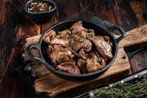 Roasted chicken liver with onions in a skillet. Wooden background. Top view photo