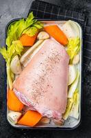 Cooking of Schweinshaxe from Raw pork shank knuckle with vegetables and herbs. Black background. Top view photo