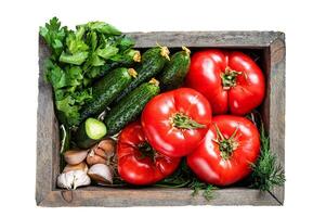 Fresh vegetables in a wooden box, red tomatoes, green cucumbers with herbs. Isolated on white background. photo