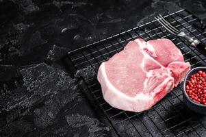 Uncooked Raw pork T bone chop meat steak on grill. Black background. Top view. Copy space photo