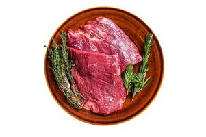 Two Flap or Flank raw beef steaks on a rustic plate with herbs. Isolated on white background. photo