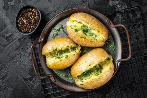 Baked Jacket potatoes with cheese, herbs and butter. Black background. Top view photo