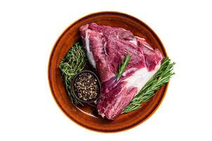 Uncooked Raw goat thigh or leg with rosemary and thyme in rustic plate. Isolated on white background. photo