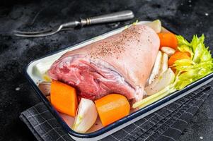 Cooking of Schweinshaxe from Raw pork shank knuckle with vegetables and herbs. Black background. Top view photo