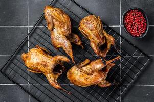 Grilled whole quails with herbs and spices. Black background. Top view photo