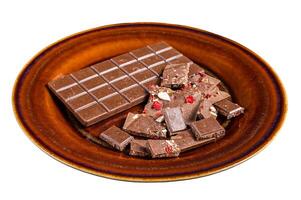 Homemade milk chocolate with hazelnuts, peanuts, cranberries and freeze dried raspberries on a rustic plate. Isolated on white background. photo