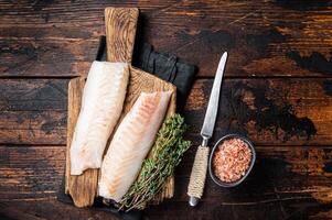 Cod fish fillets, raw codfish with thyme on wooden board. Wooden background. Top view photo