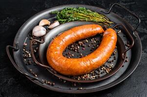 Smoked sausage with thyme and spices in a steel tray. Black background. Top view photo
