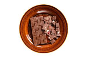 Homemade milk chocolate with hazelnuts, peanuts, cranberries and freeze dried raspberries on a rustic plate. Isolated on white background. photo