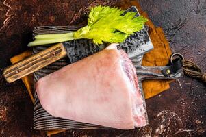 Fresh Raw pork shank knuckle on a butcher board with herbs for cooking. Dark background. Top view photo