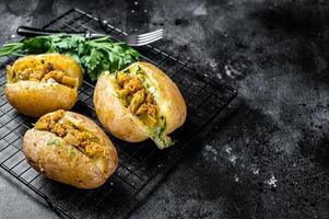 Turkish Kumpir, baked potatoes stuffed with cheese, bacon, salty cucumber, herbs and butter. Black background. Top view. Copy space photo