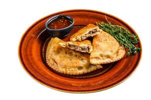Fried empanadas with minced beef meat served on a plate with chili sauce. Isolated on white background. photo