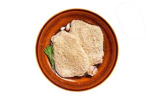 Raw Breaded German Wiener schnitzel on a rustic plate with herbs. Isolated on white background. photo