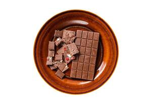Homemade milk chocolate with hazelnuts, peanuts, cranberries and freeze dried raspberries on a rustic plate. Isolated, white background. Top view. photo