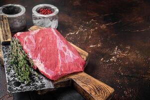 Alternative raw flap flank beef meat steak on butcher board. Dark background. Top view. Copy space photo
