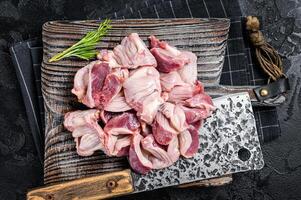 Raw chicken stomachs, giblets gizzards on a butcher board with meat cleaver. Black background. Top view photo