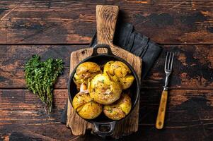 Crushed, Broken potatoes baked in oil with herbs. Wooden background. Top view photo