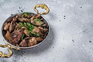 Chicken liver stew with onions and parsley in a skillet. Gray background. Top view. Copy space photo