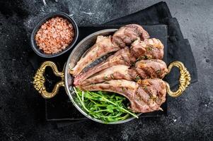 Grilled Lamb mutton Chops steaks in a skillet with green salad. Black background. Top view photo