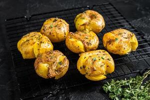 Crushed, smashed potatoes baked with rosemary and thyme. Black background. Top view photo